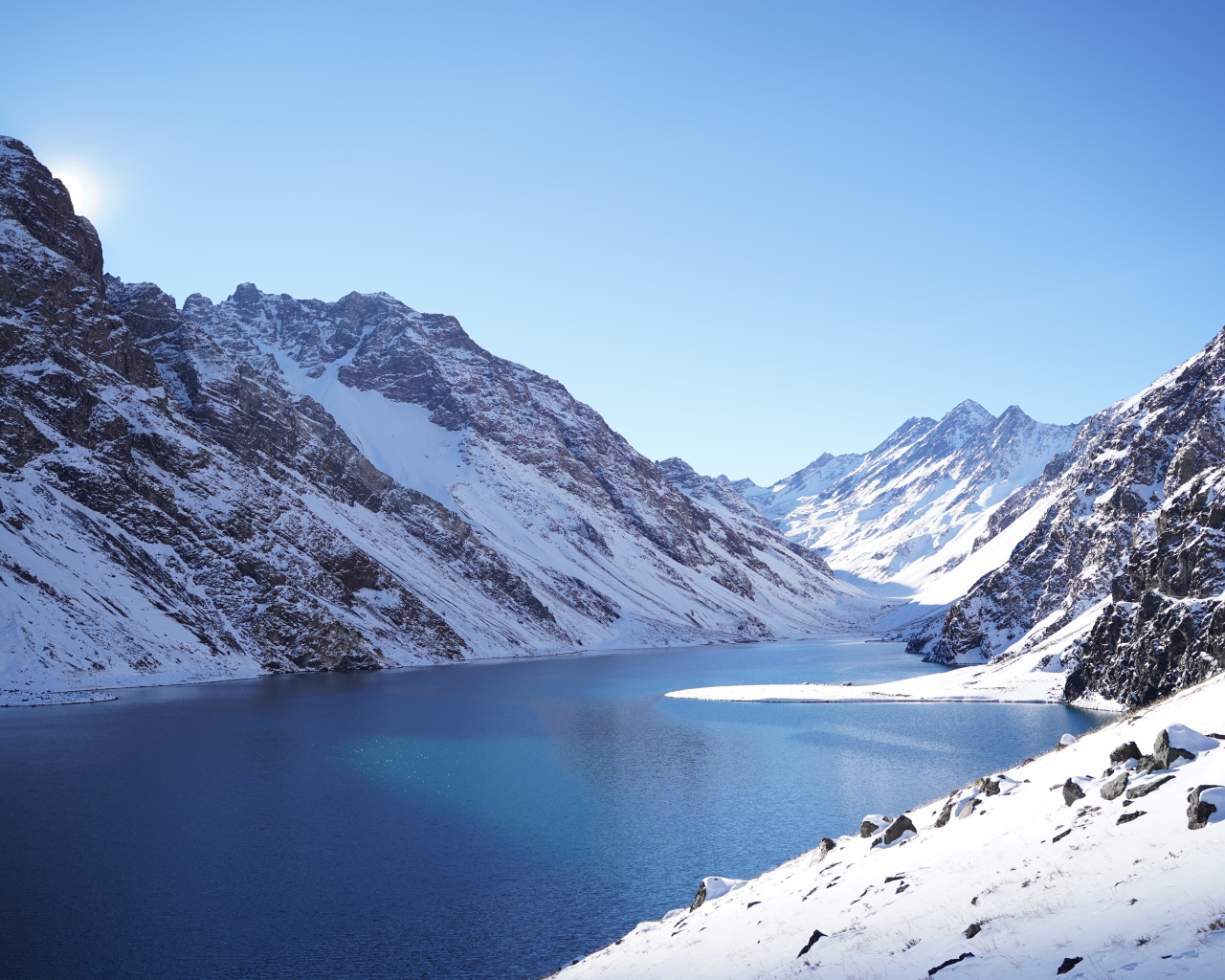 Озеро у покрытых снегом гор под голубым небом