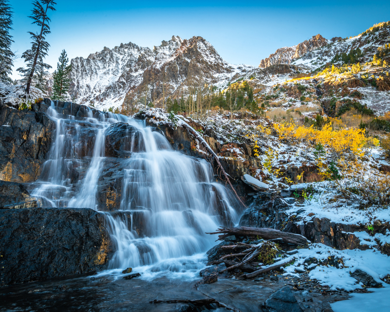 Красивый водопад стекает по холодным камням на фоне заснеженных гор