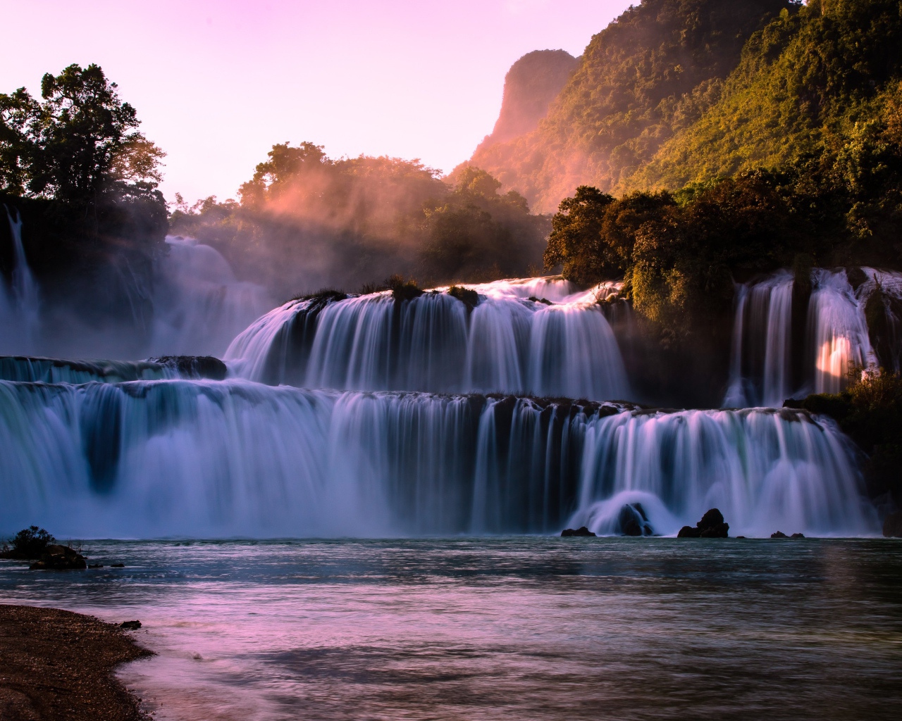 Каскадный водопад стекает по камням в лучах солнца 