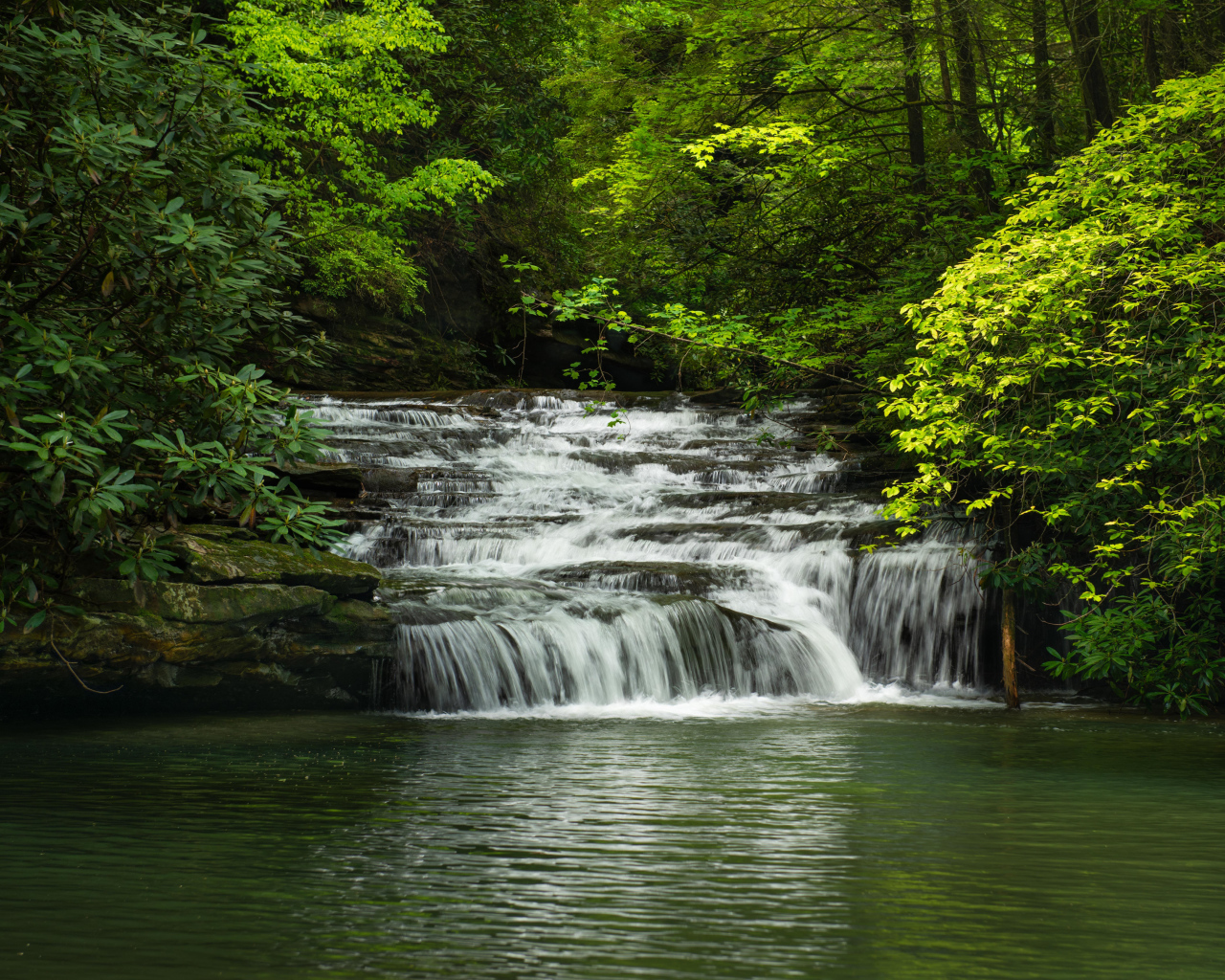 Водопад стекает по каменному каскаду в реку 