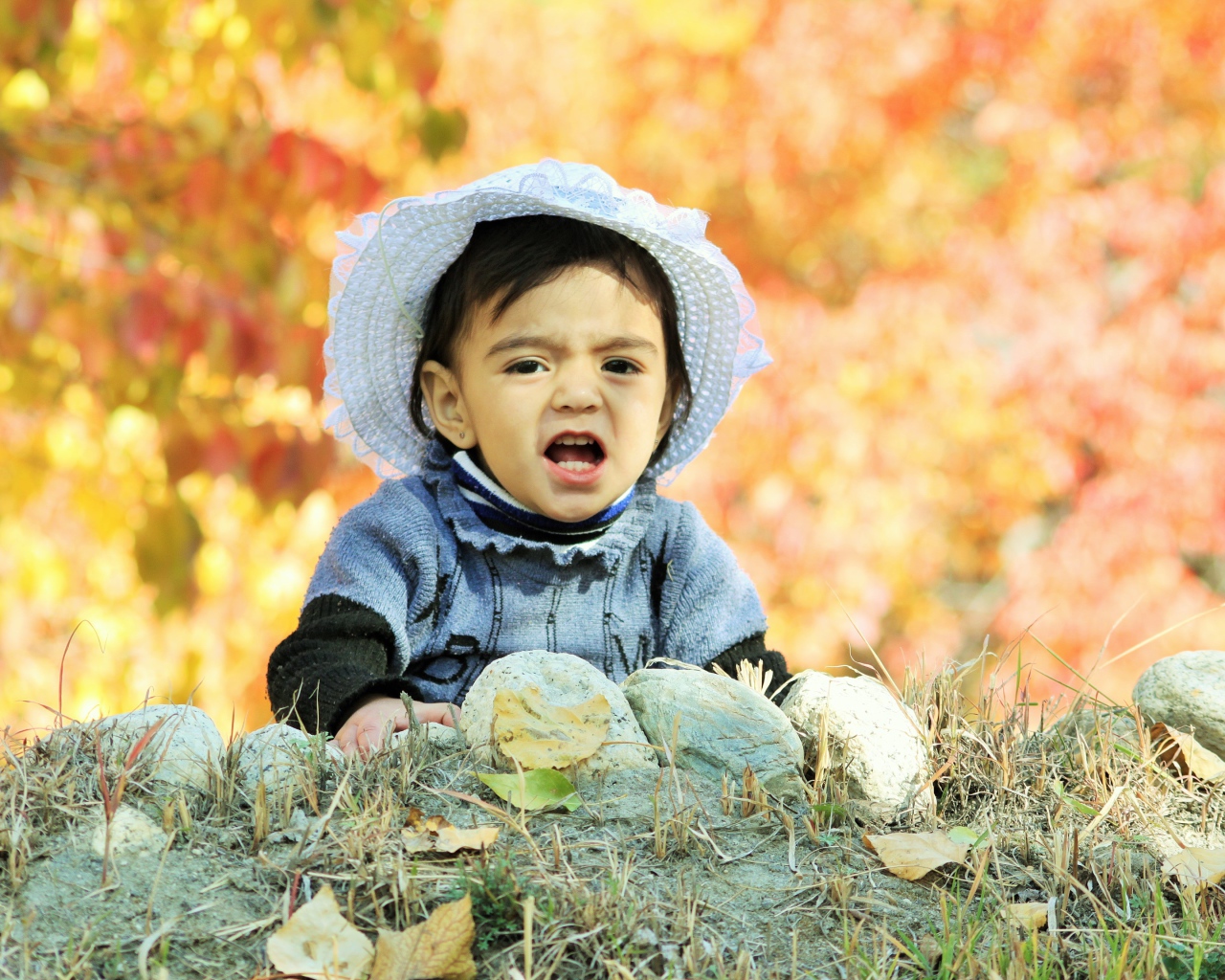 Маленькая девочка в шляпке сидит на земле