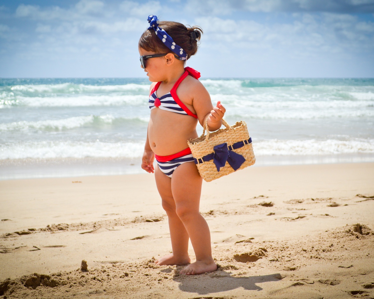 Маленькая девочка в купальнике гуляет по пляжу 