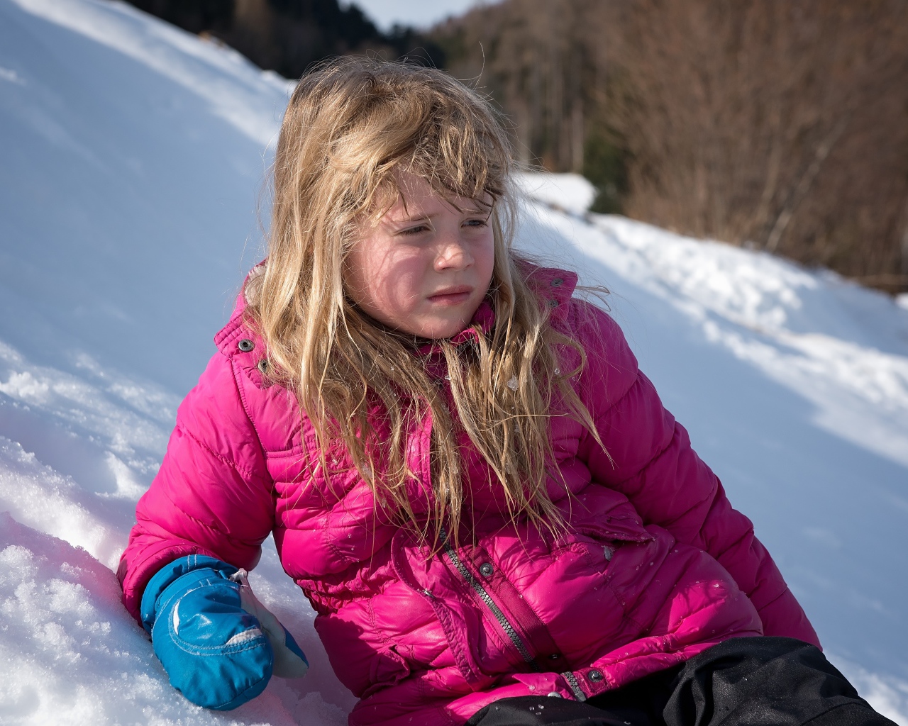 Маленькая девочка лежит на заснеженной горке 