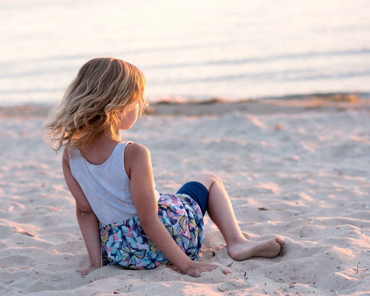 Маленькая девочка лежит на песке на закате 