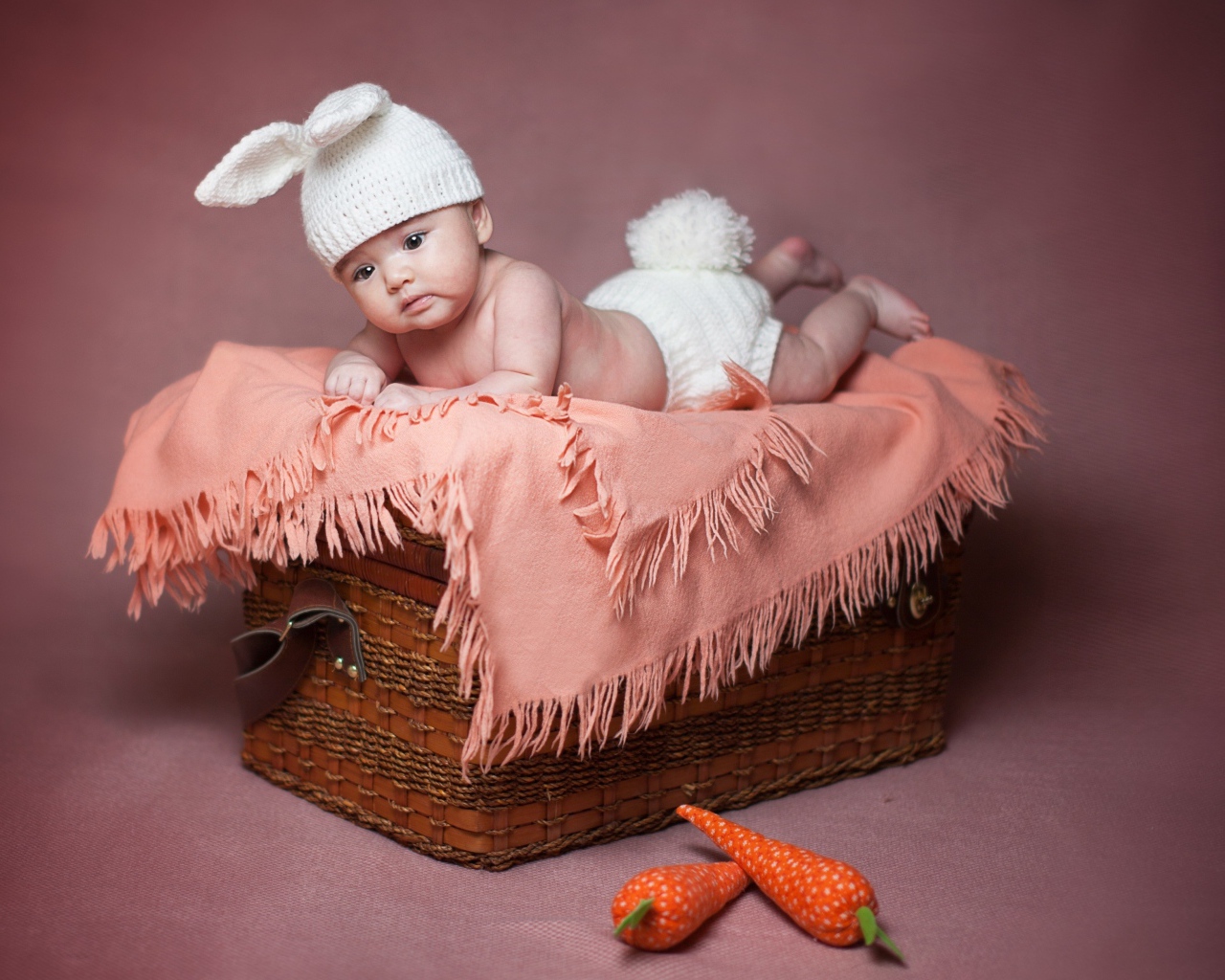 Маленький ребенок в костюме зайчика лежит на корзине 