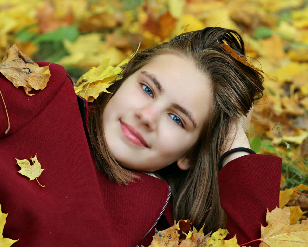 Красивая голубоглазая девочка лежит на опавшей листве