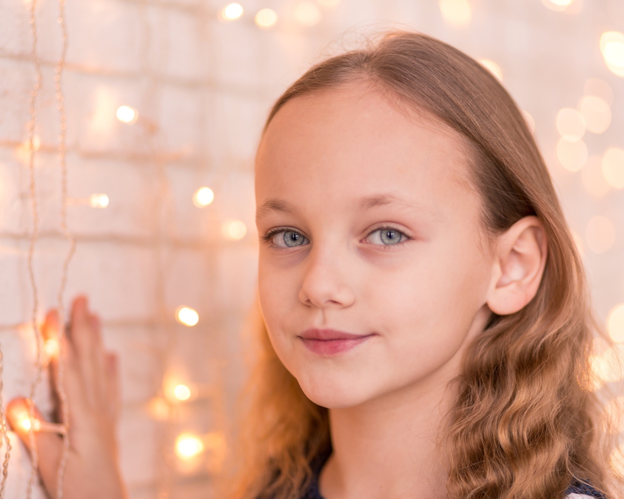 Красивая голубоглазая девочка стоит у стены с гирляндой