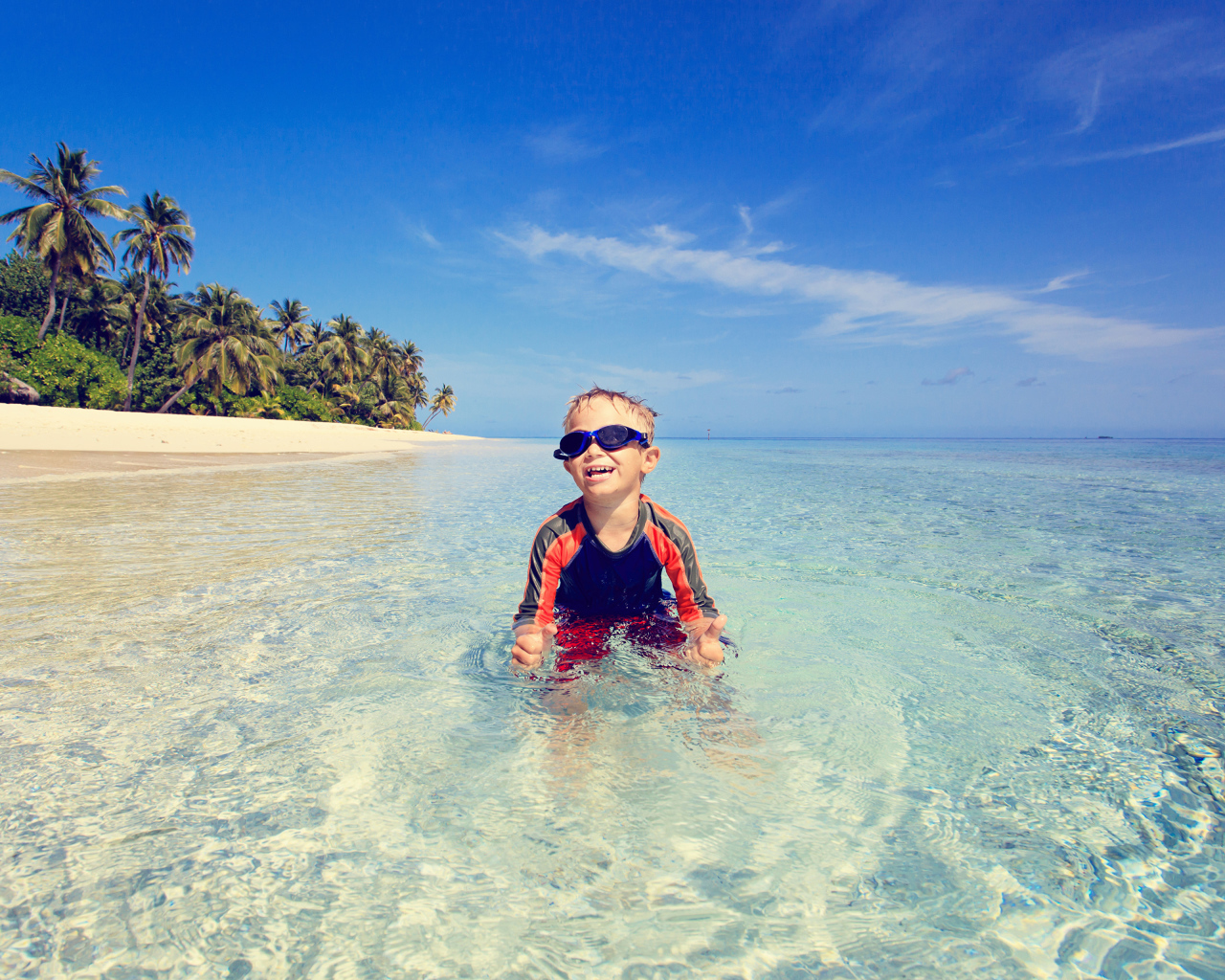 Мальчик в очках сидит в воде на пляже 
