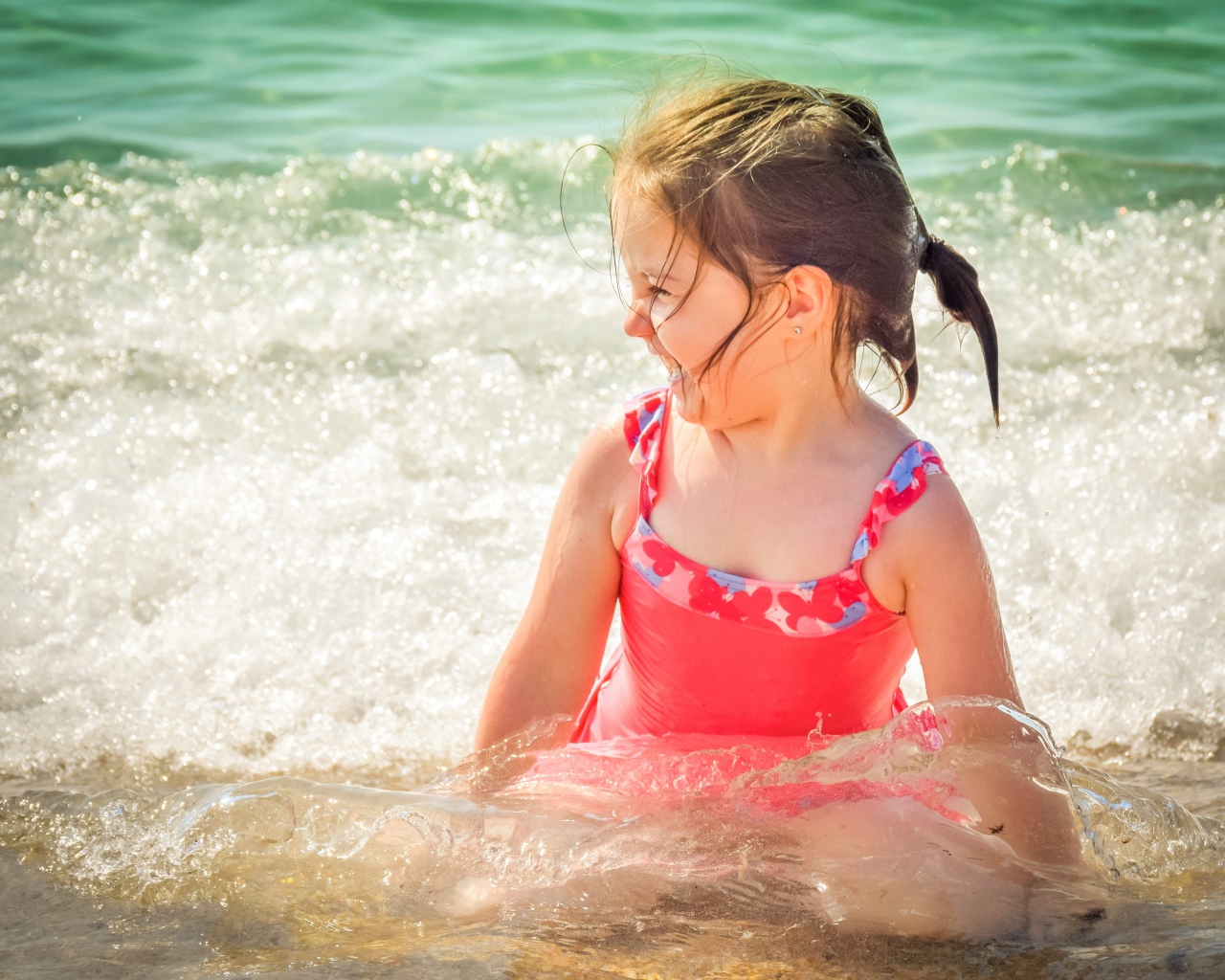 Веселая маленькая девочка в купальнике сидит в воде 