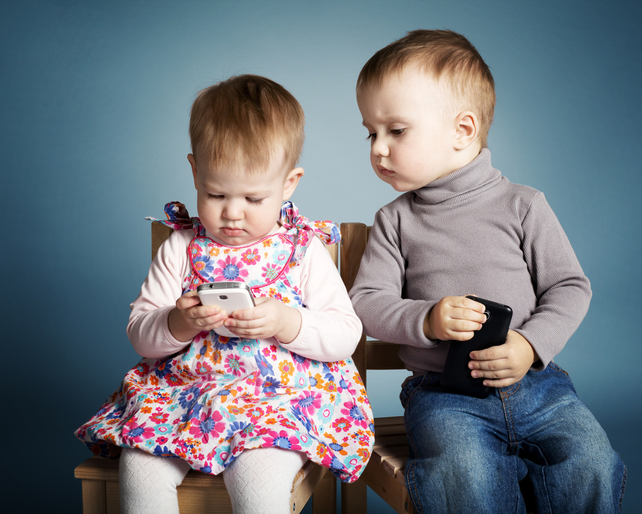 Маленькие мальчик  и девочка с телефонами на сером фоне 