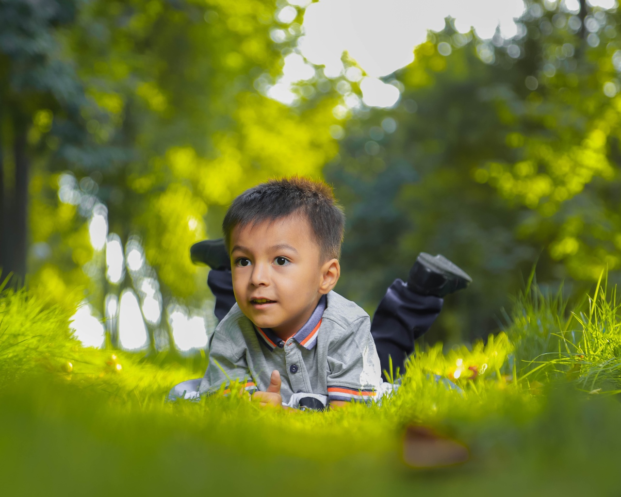 Маленький мальчик лежит на зеленой траве 