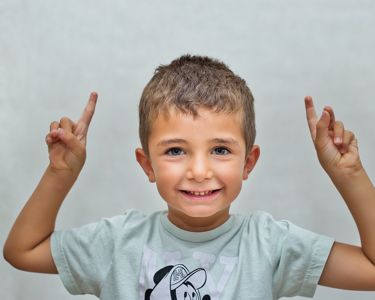 Маленький мальчик поднял руки вверх на сером фоне