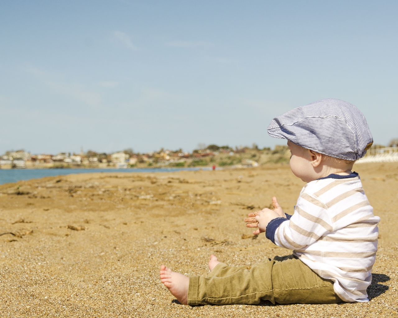 Маленький мальчик сидит на песке у реки