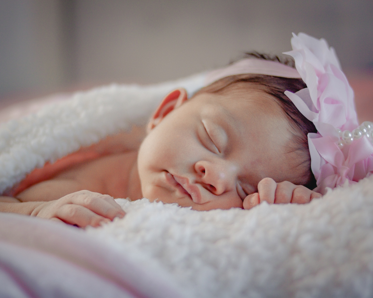 Маленькая грудная девочка с цветком на голове на кровати 