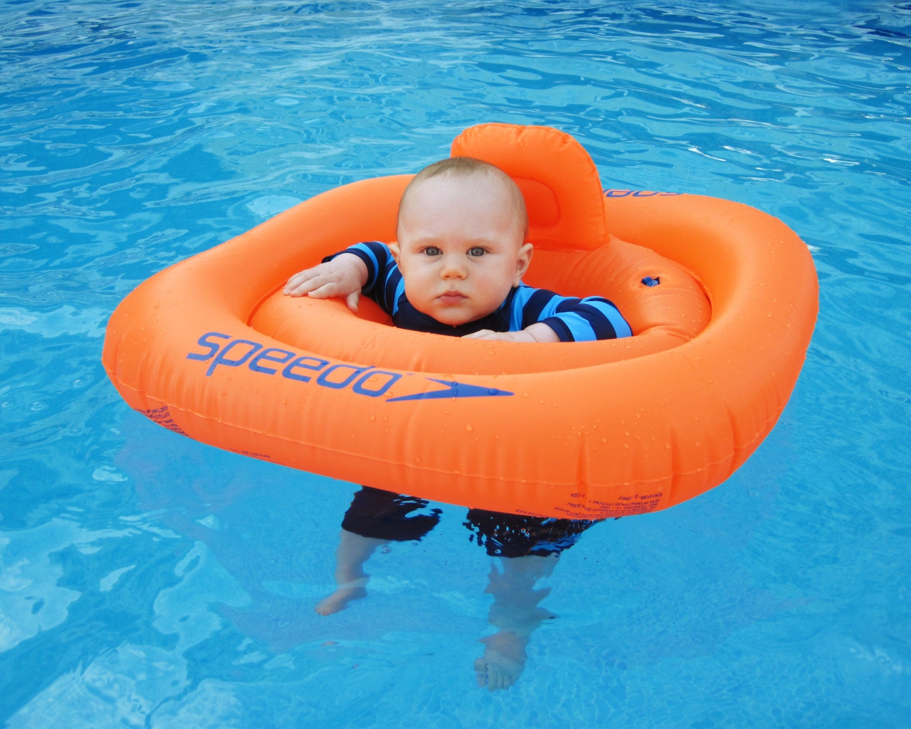 Маленький ребенок с оранжевым спасательным кругом в бассейне