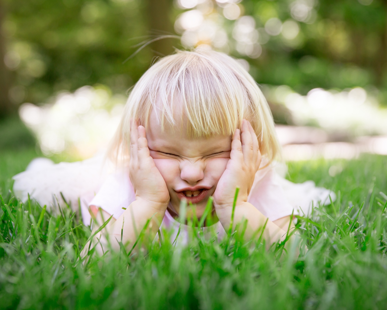 Маленькая смешная девочка лежит на зеленой траве 