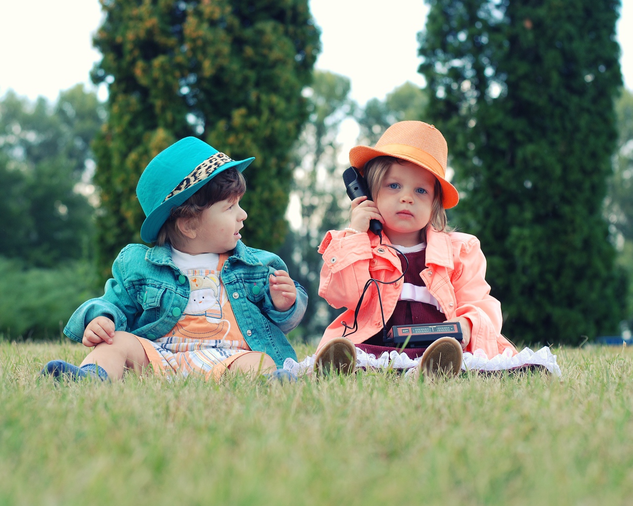 Маленькие девочка и мальчик сидят на траве с телефоном 