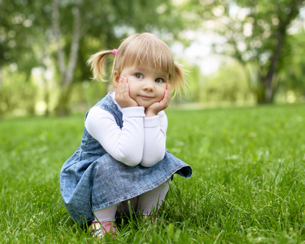 Маленькая девочка в сарафане сидит на траве 