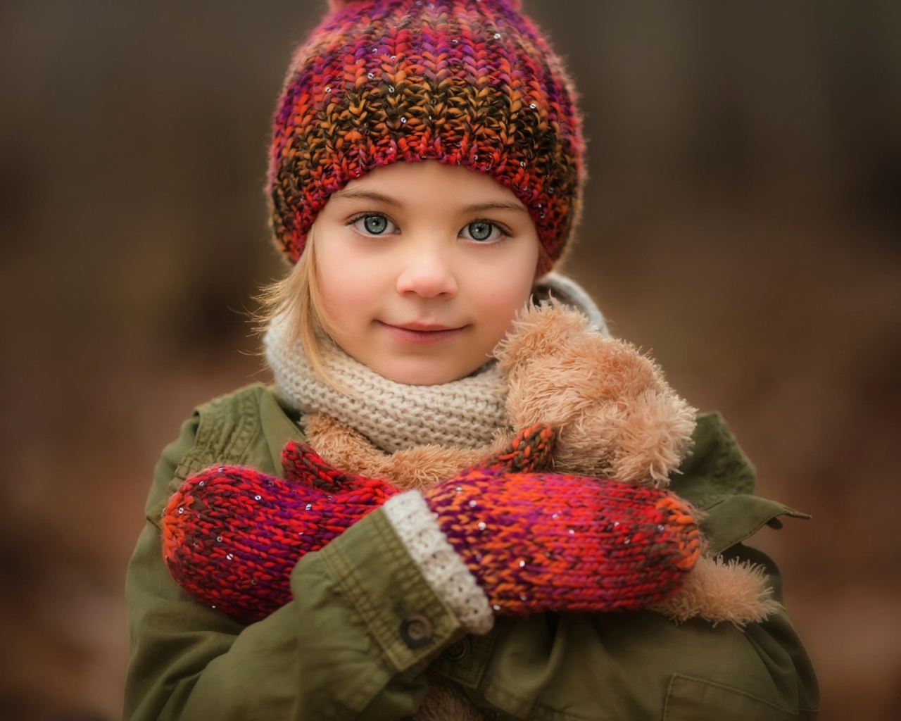 Маленькая девочка в теплой шапке и варежках  с игрушкой в руках 