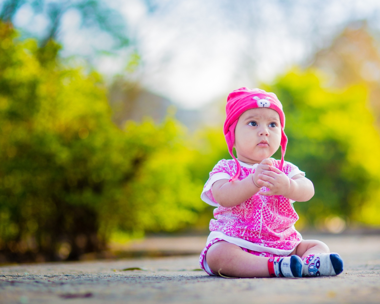 Маленькая девочка в розовом костюме сидит на земле