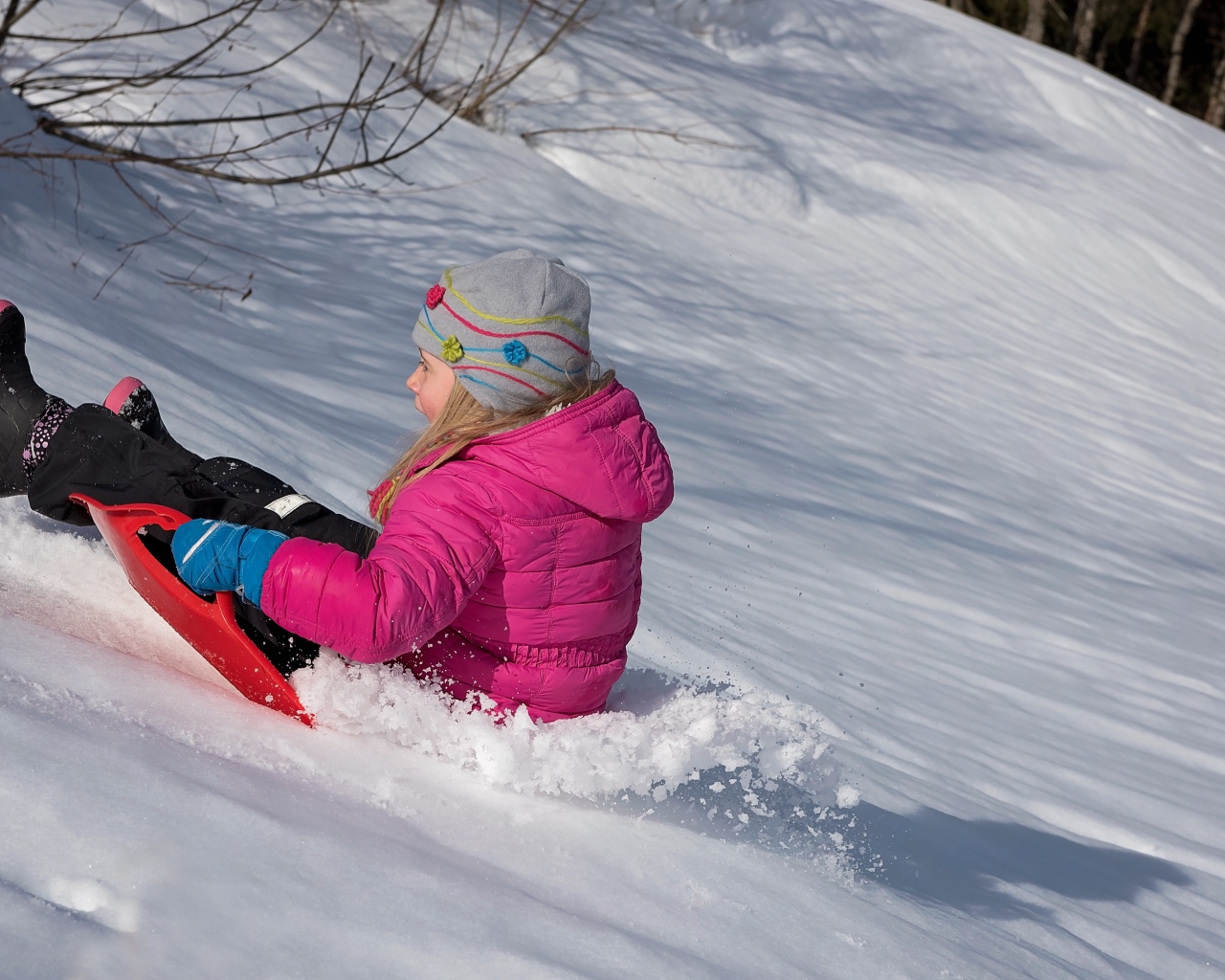 Маленькая девочка катится с заснеженной горки 