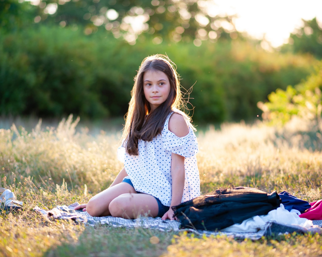 Маленькая девочка сидит на покрывале на земле 