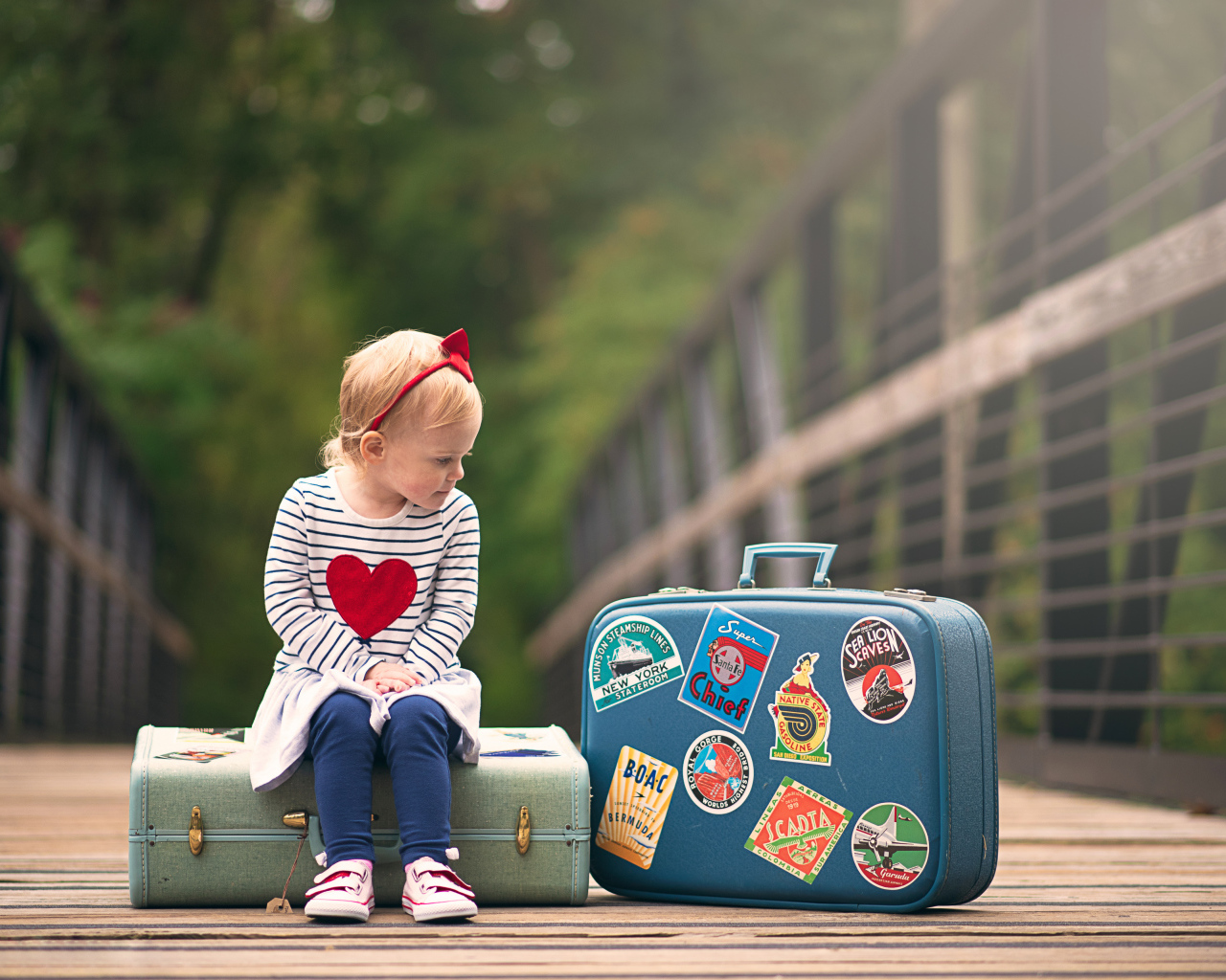 Маленькая девочка сидит на мосту с чемоданами