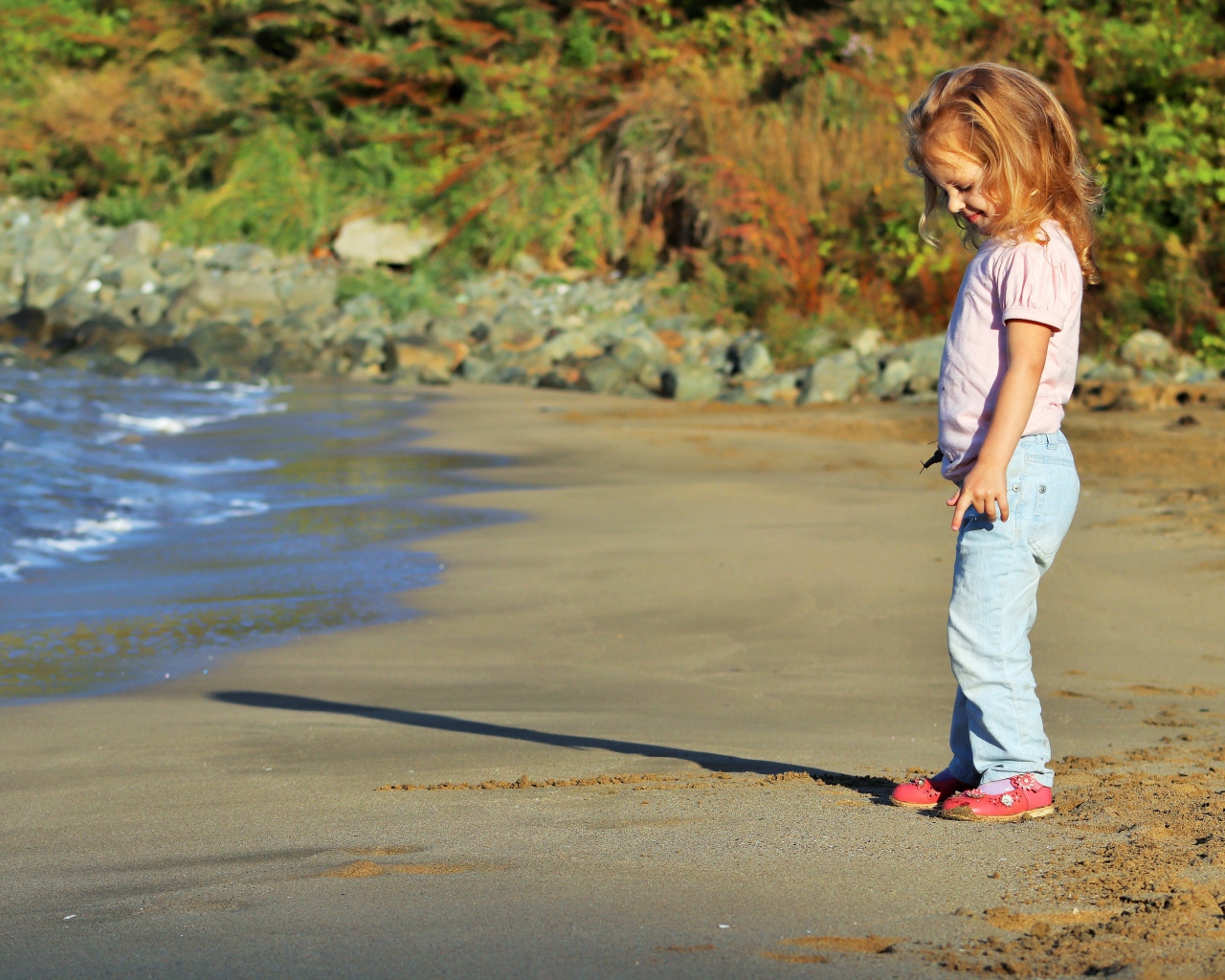 Маленькая девочка гуляет по мокрому песку 