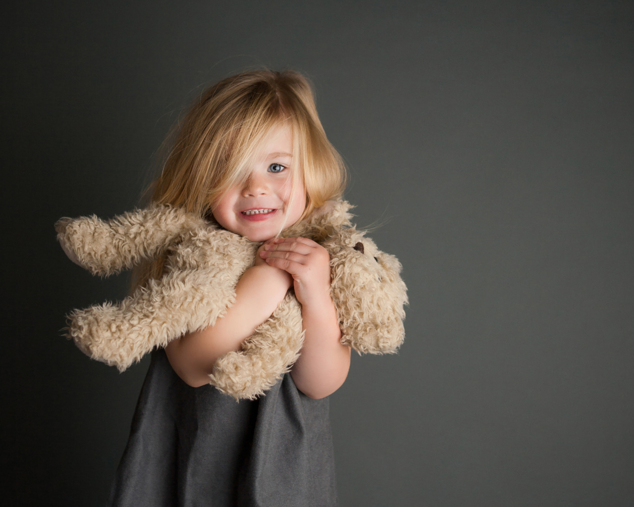 Маленькая девочка с игрушечным медвежонком в руках  на сером фоне 