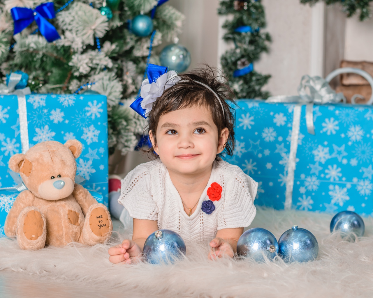 Маленькая девочка с подарками и игрушками под елкой 