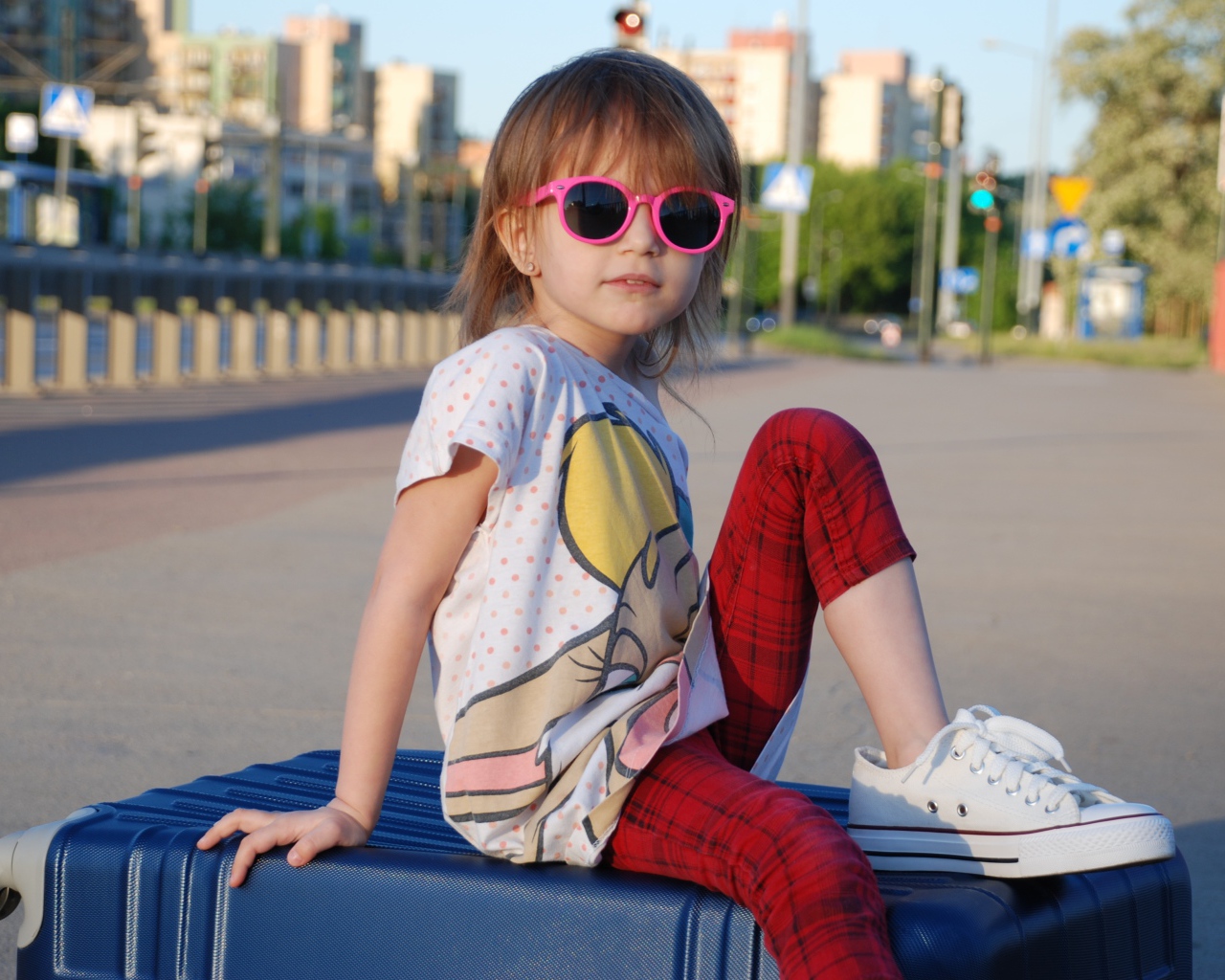 Маленькая девочка в очках сидит на чемодане