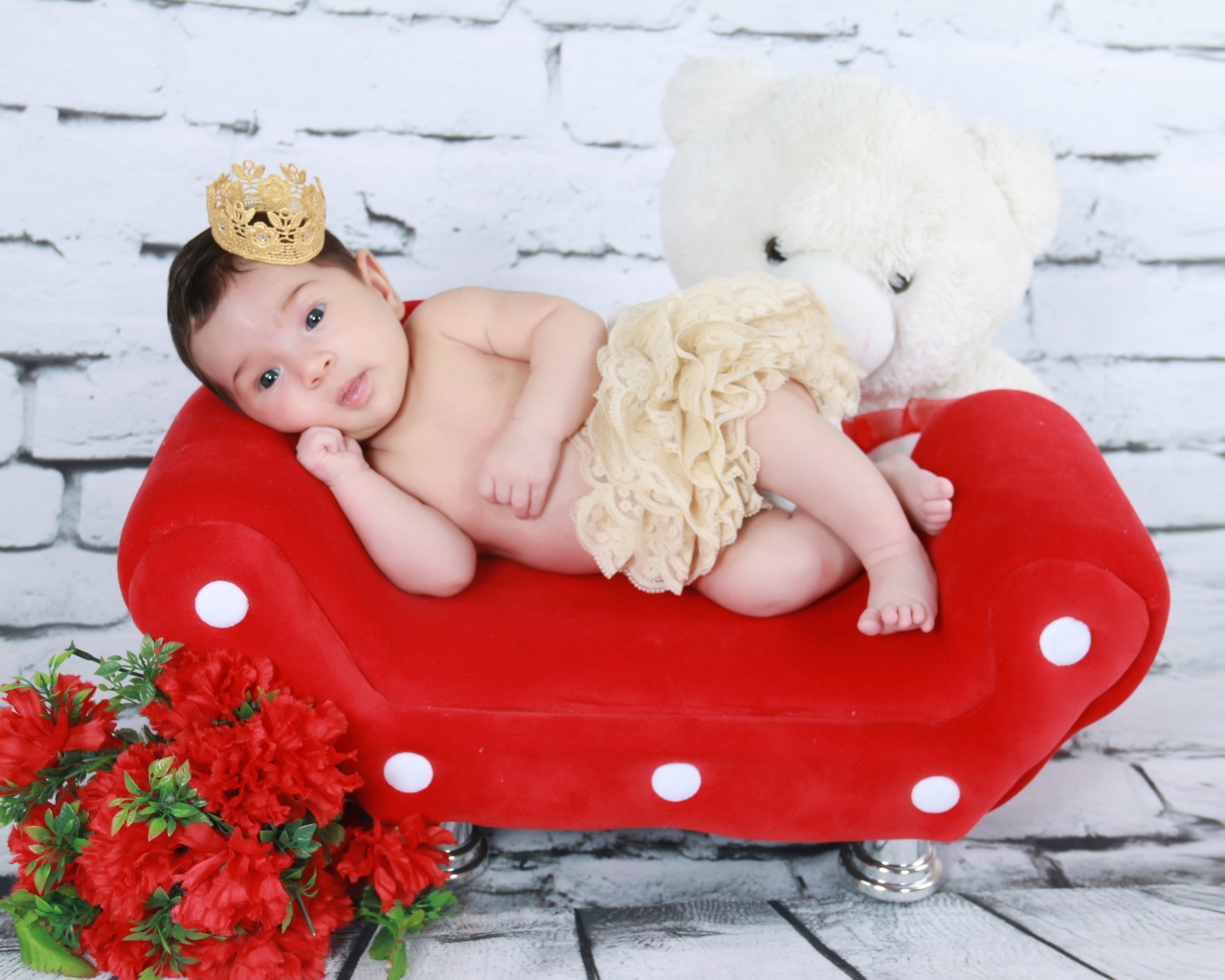 Маленькая принцесса лежит на красном диване у стены 