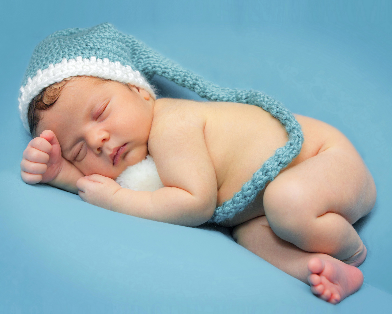 Маленький спящий ребенок в шапке на голубом фоне 