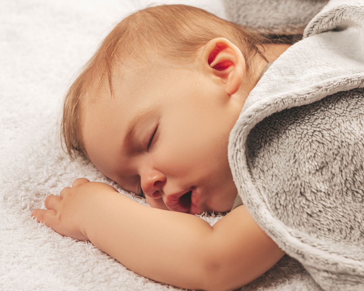 Маленький спящий ребенок под серым покрывалом 