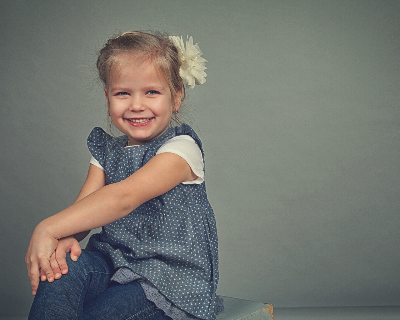 Маленькая улыбающаяся девочка с бантом на сером фоне 