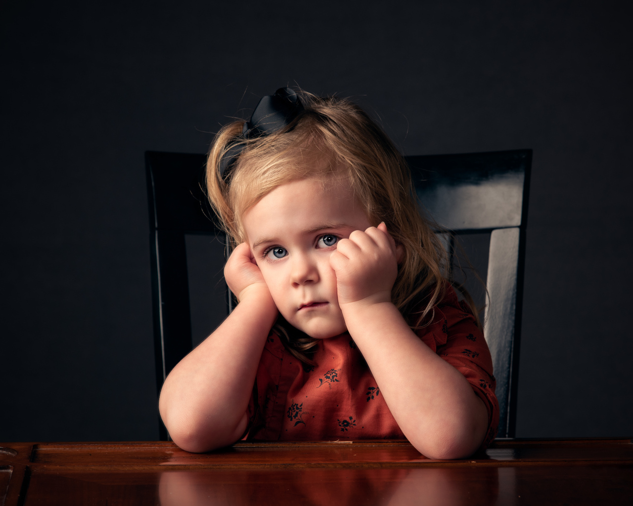 Грустная маленькая девочка сидит за столом