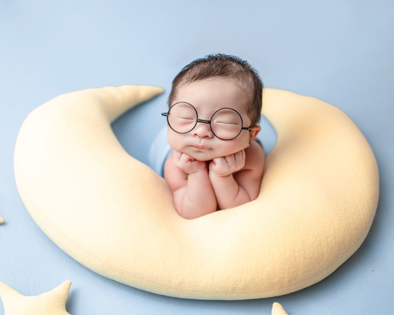 Спящий грудной ребенок в очках на желтой подушке 