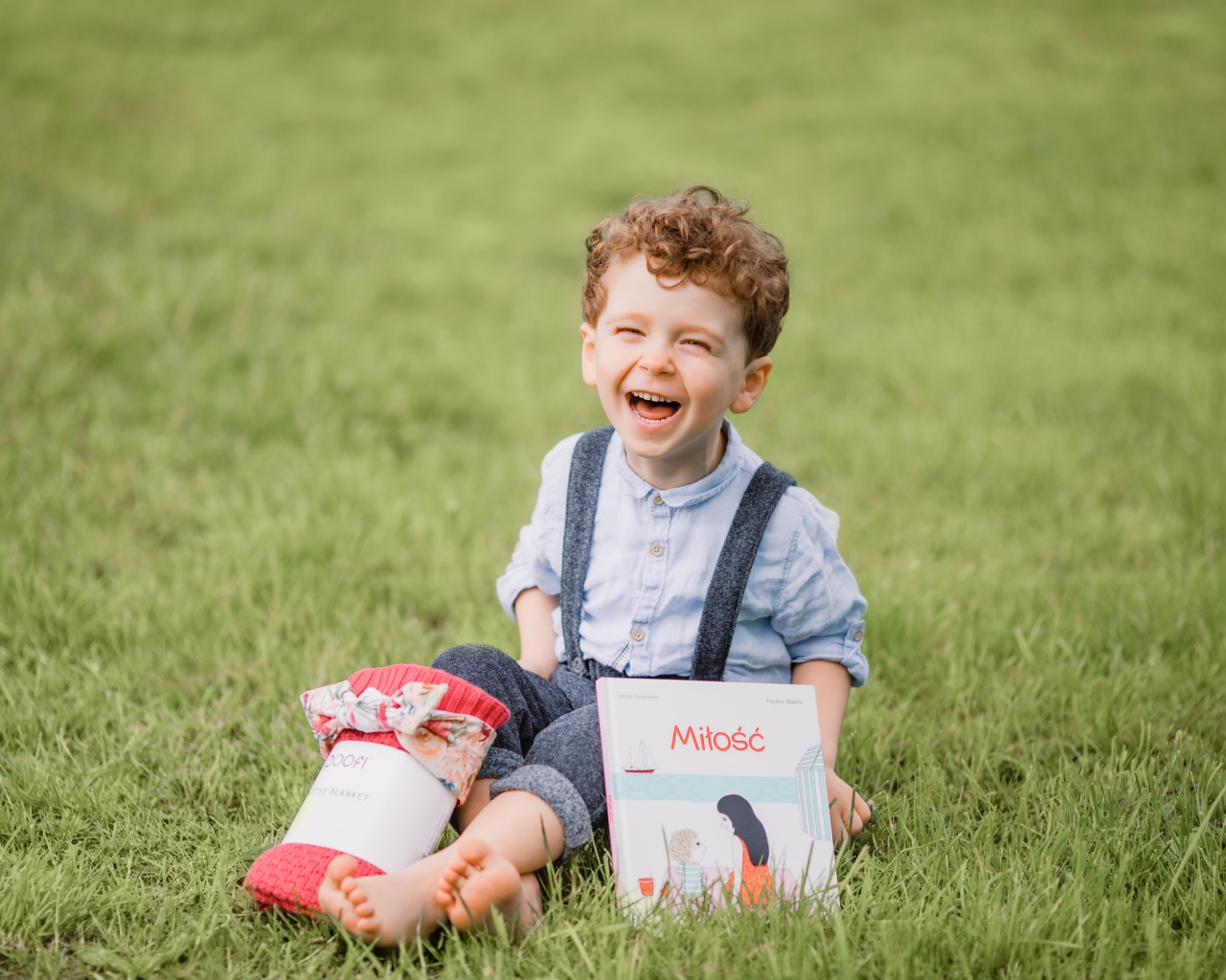 Улыбающийся маленький мальчик сидит на зеленой траве