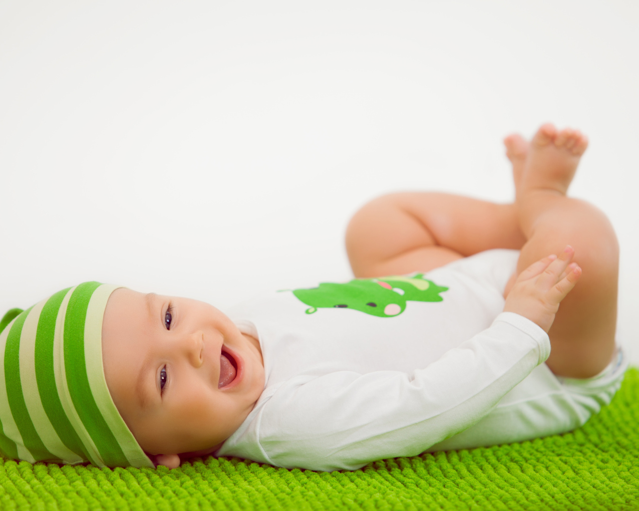 Улыбающийся маленький ребенок лежит на зеленом покрывале 