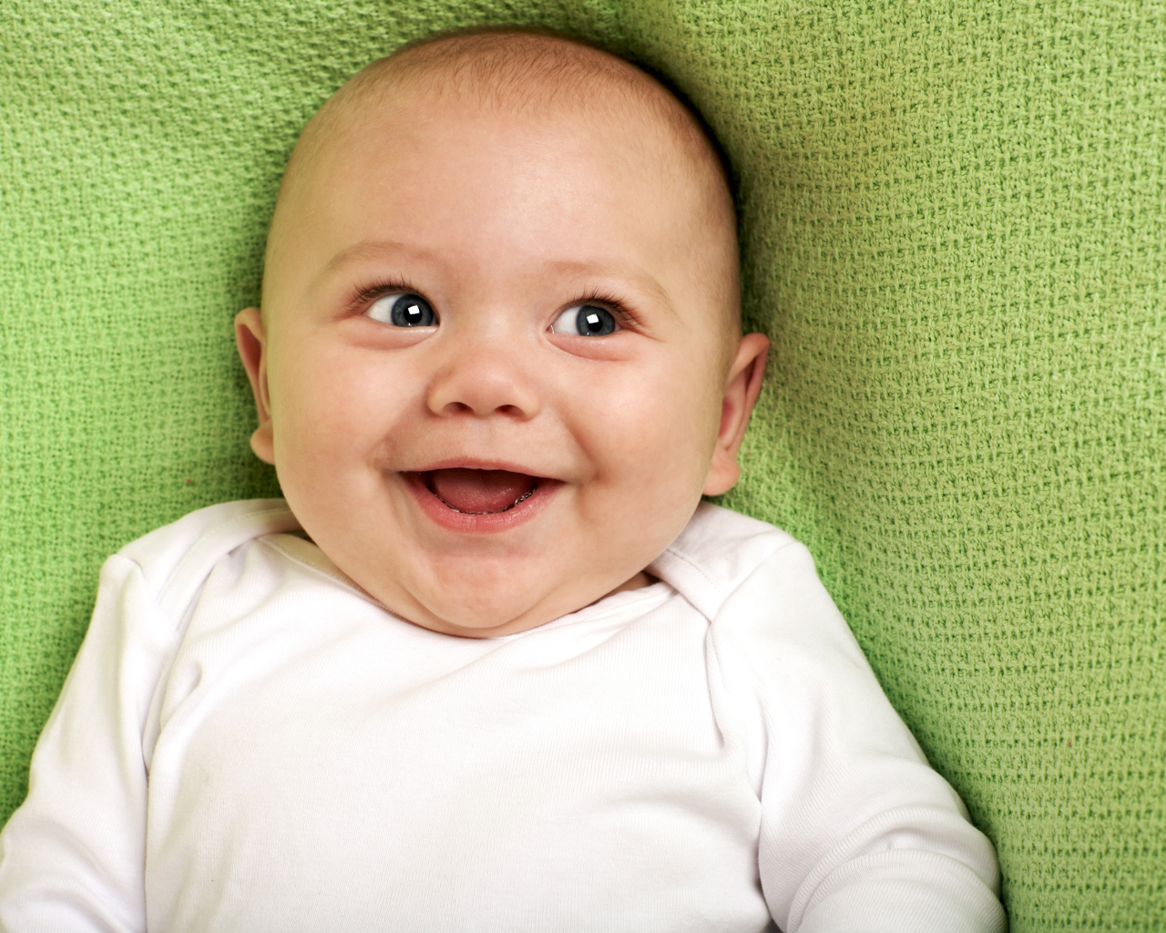 Улыбающийся маленький ребенок на зеленом покрывале 