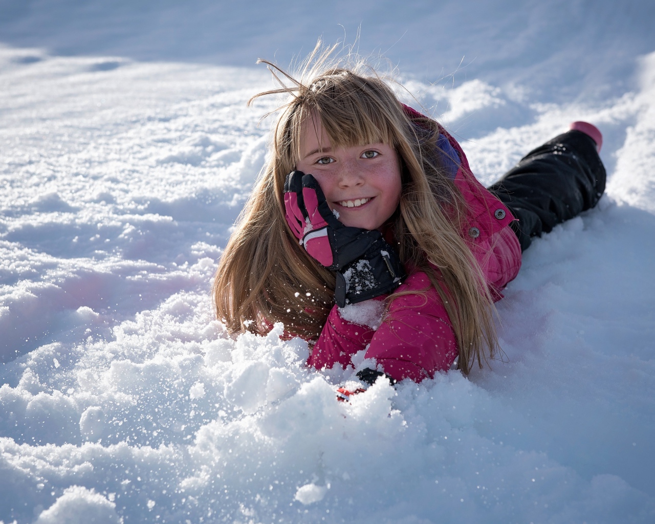 Улыбающаяся маленькая девочка лежит на снегу