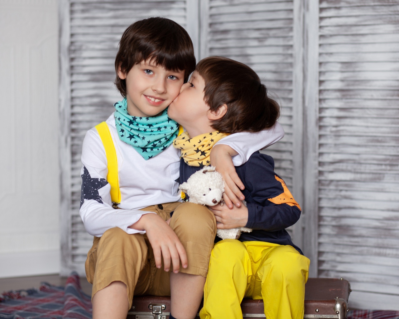 Два маленьких брата сидят на чемодане у стены