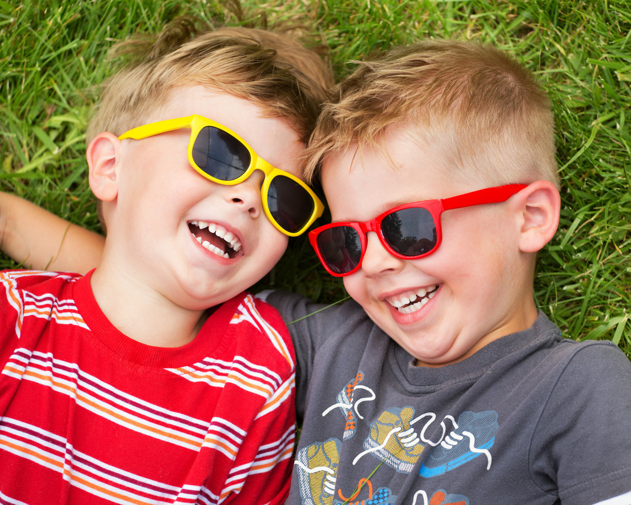 Два улыбающихся мальчика в очках на зеленой траве 