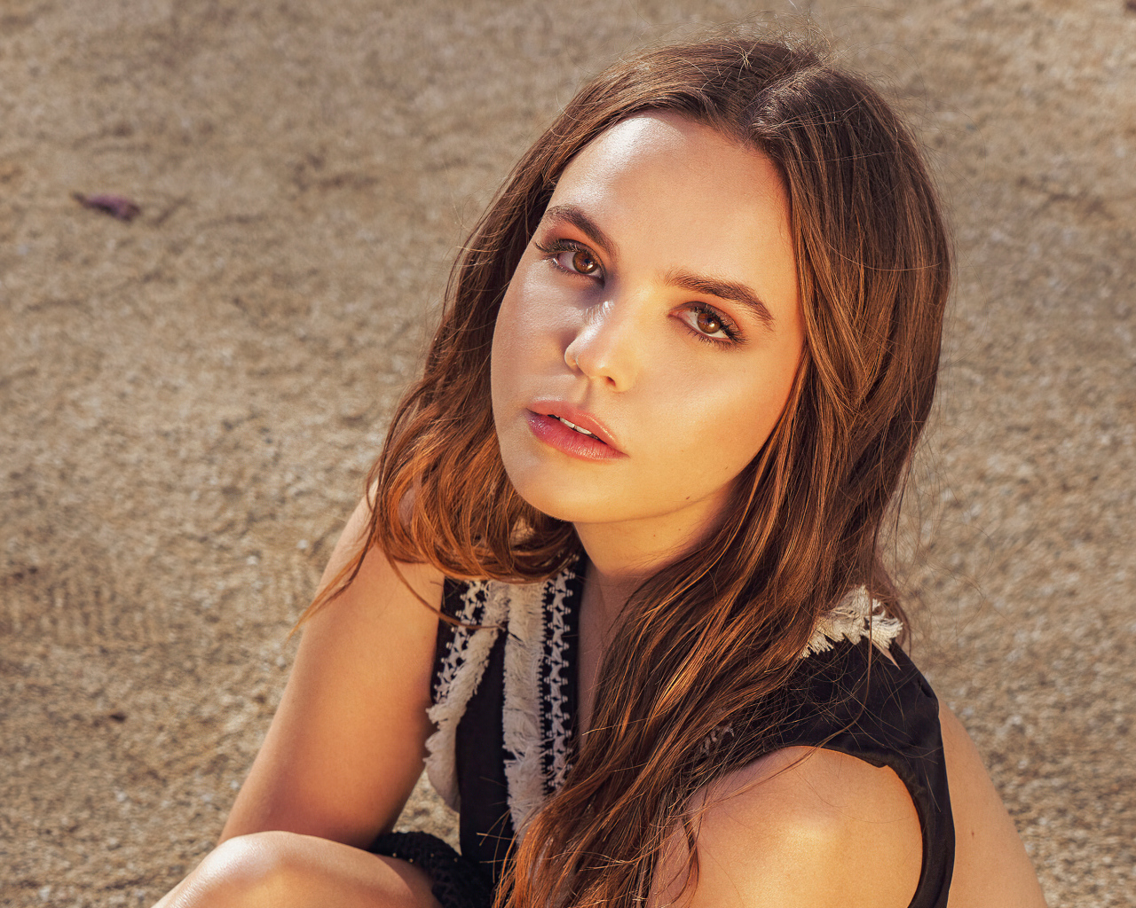 Кареглазая актриса Бэйли Мэдисон сидит на песке