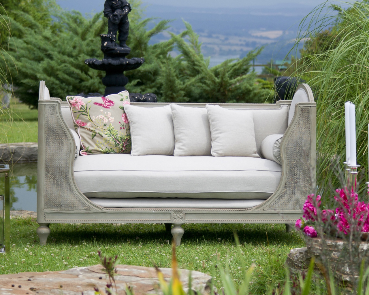 Большой серый диван в саду у пруда 