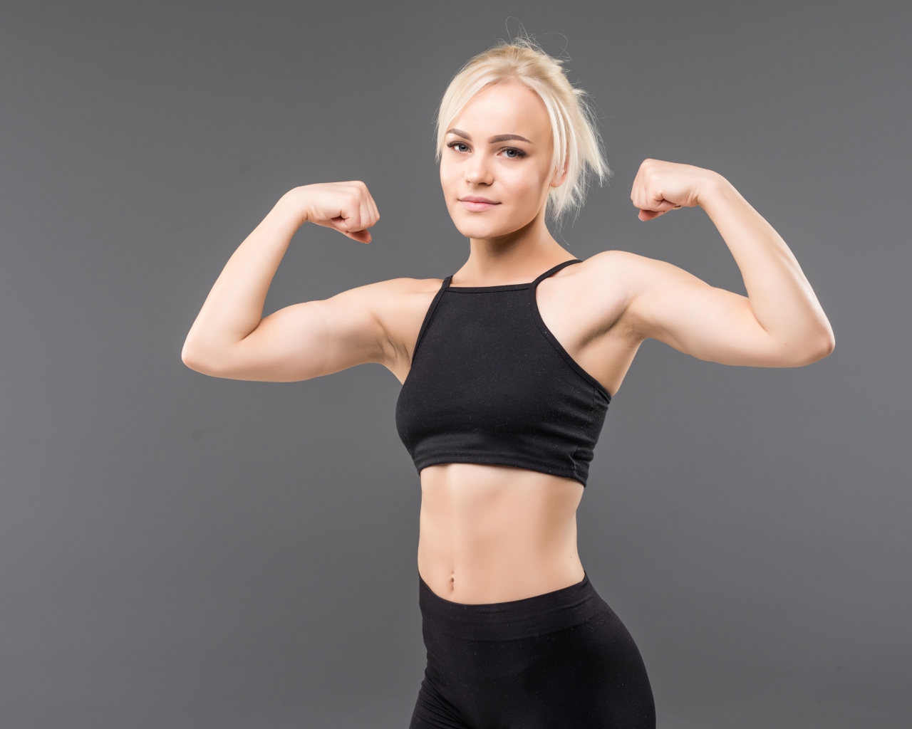 Спортивная блондинка в черном костюме на сером фоне