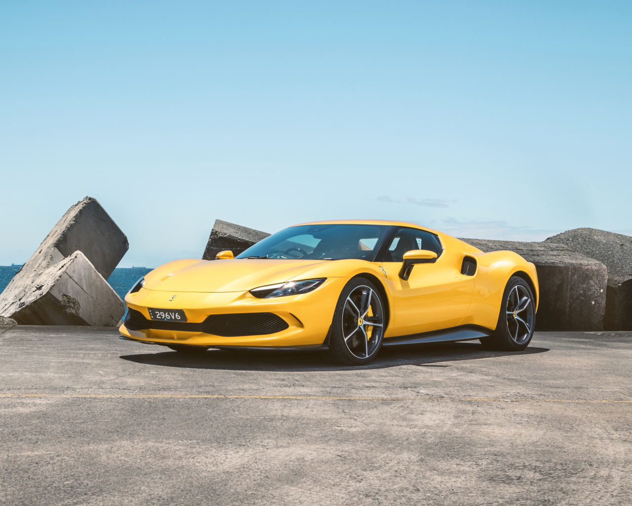 Желтый автомобиль Ferrari 296 GTB у камней