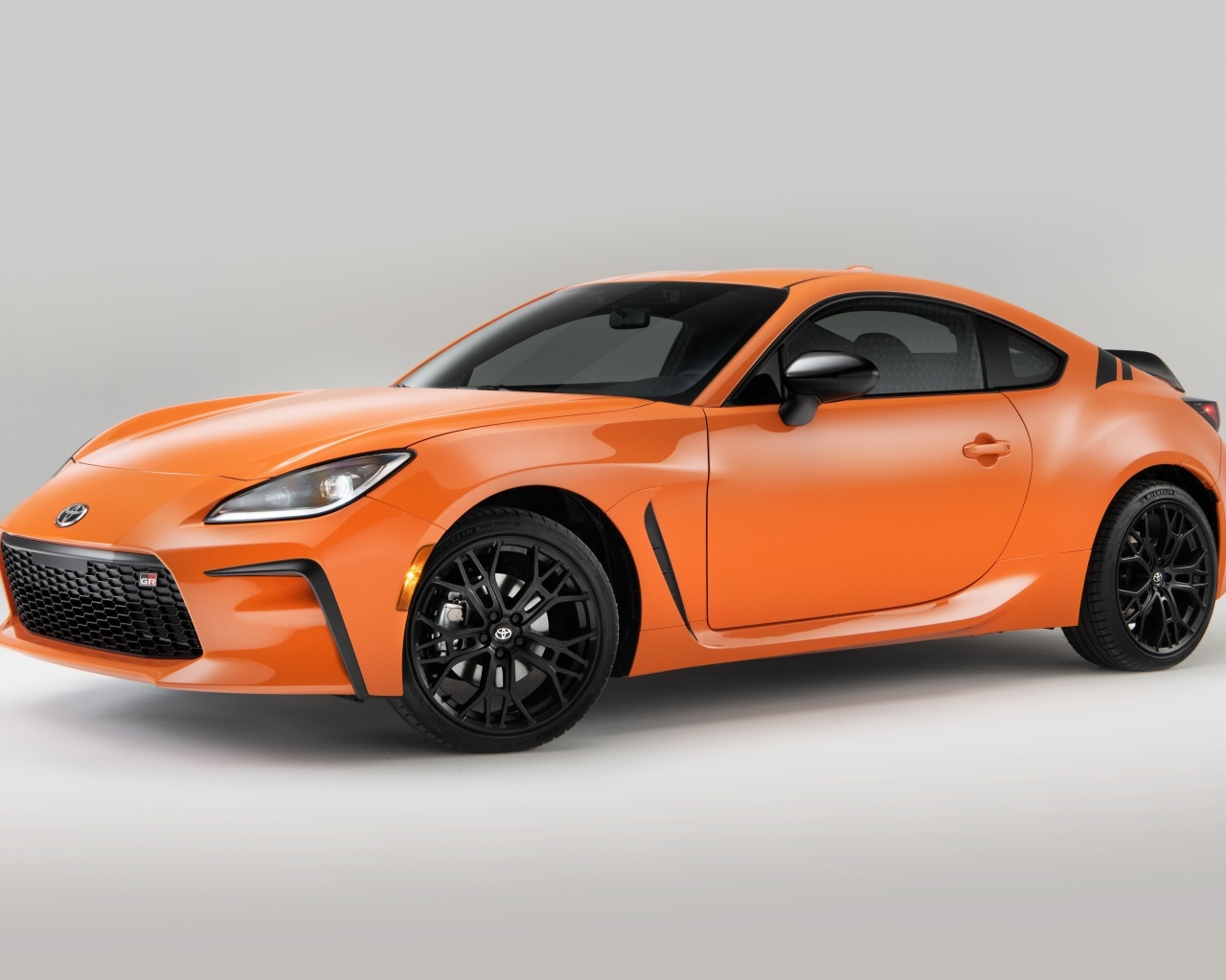 Оранжевый автомобиль Toyota GR 86 на сером фоне