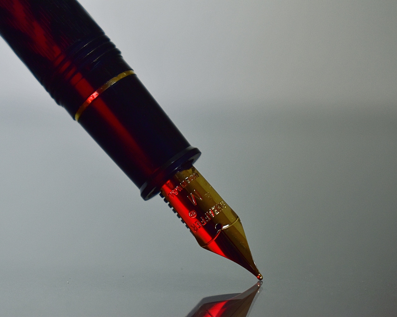 Золотое перо чернильной ручки на сером фоне