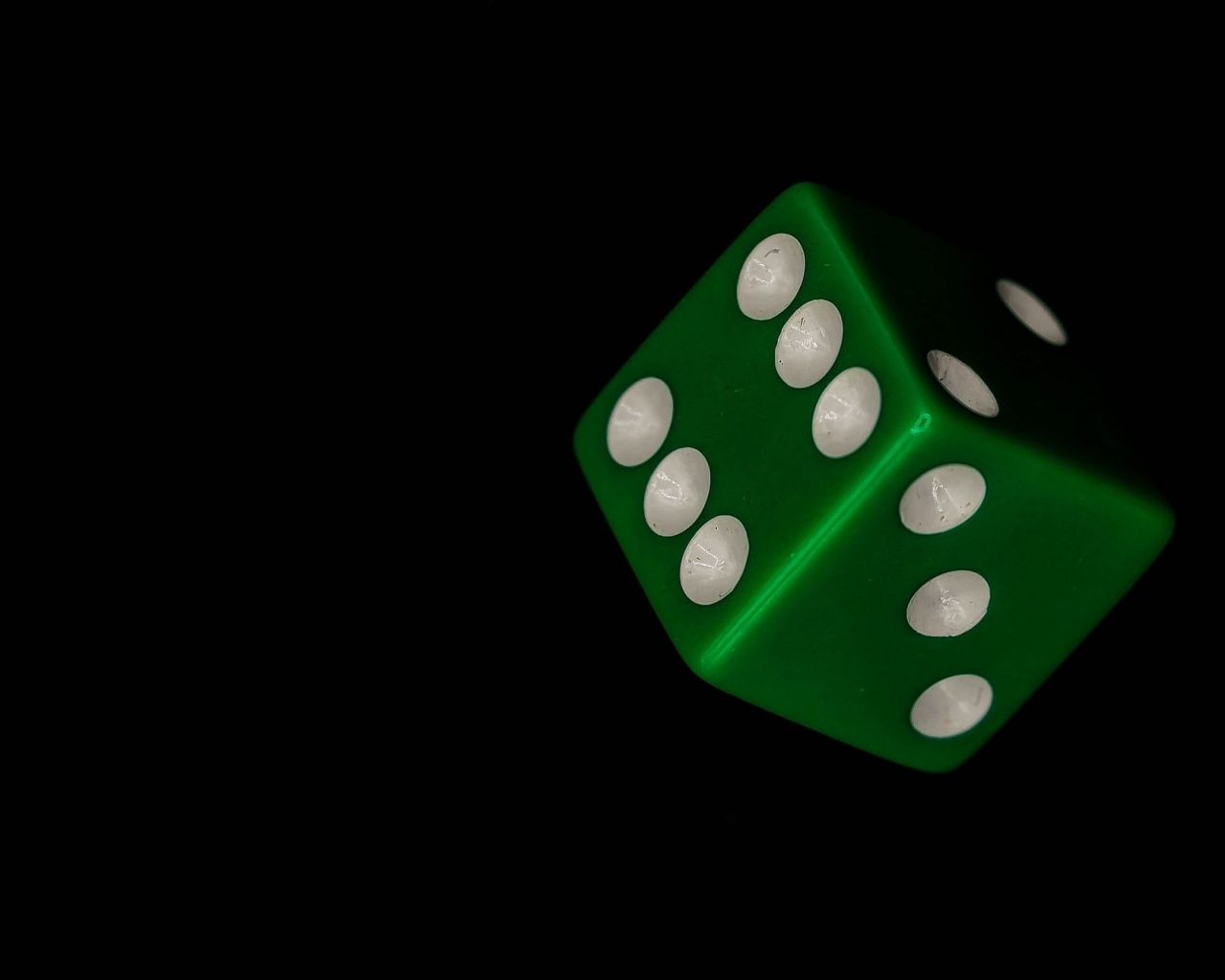 Зеленый игральный кубик на черном фоне
